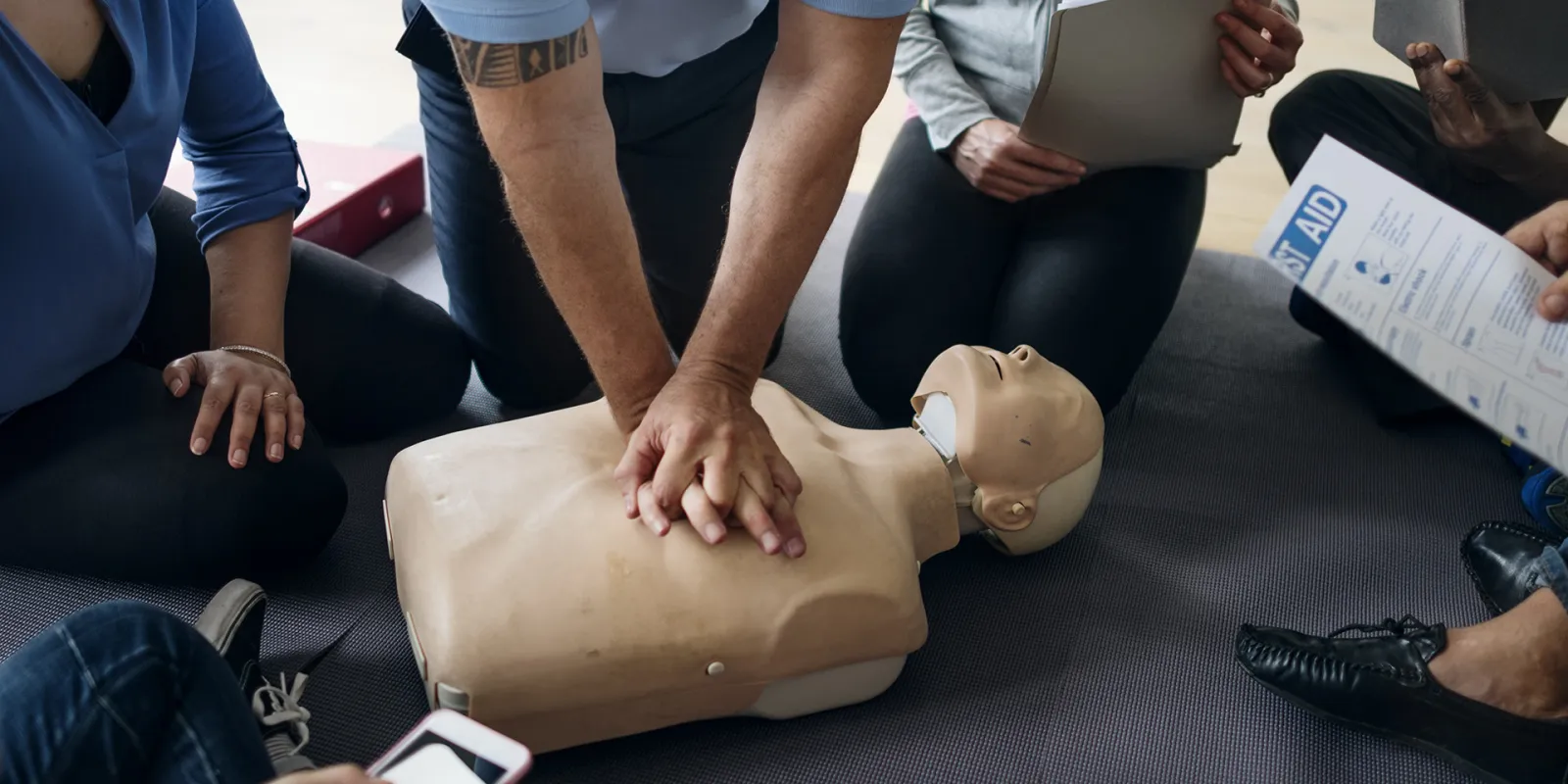 Learners watching an instructor demonstrate CPR on a manikin